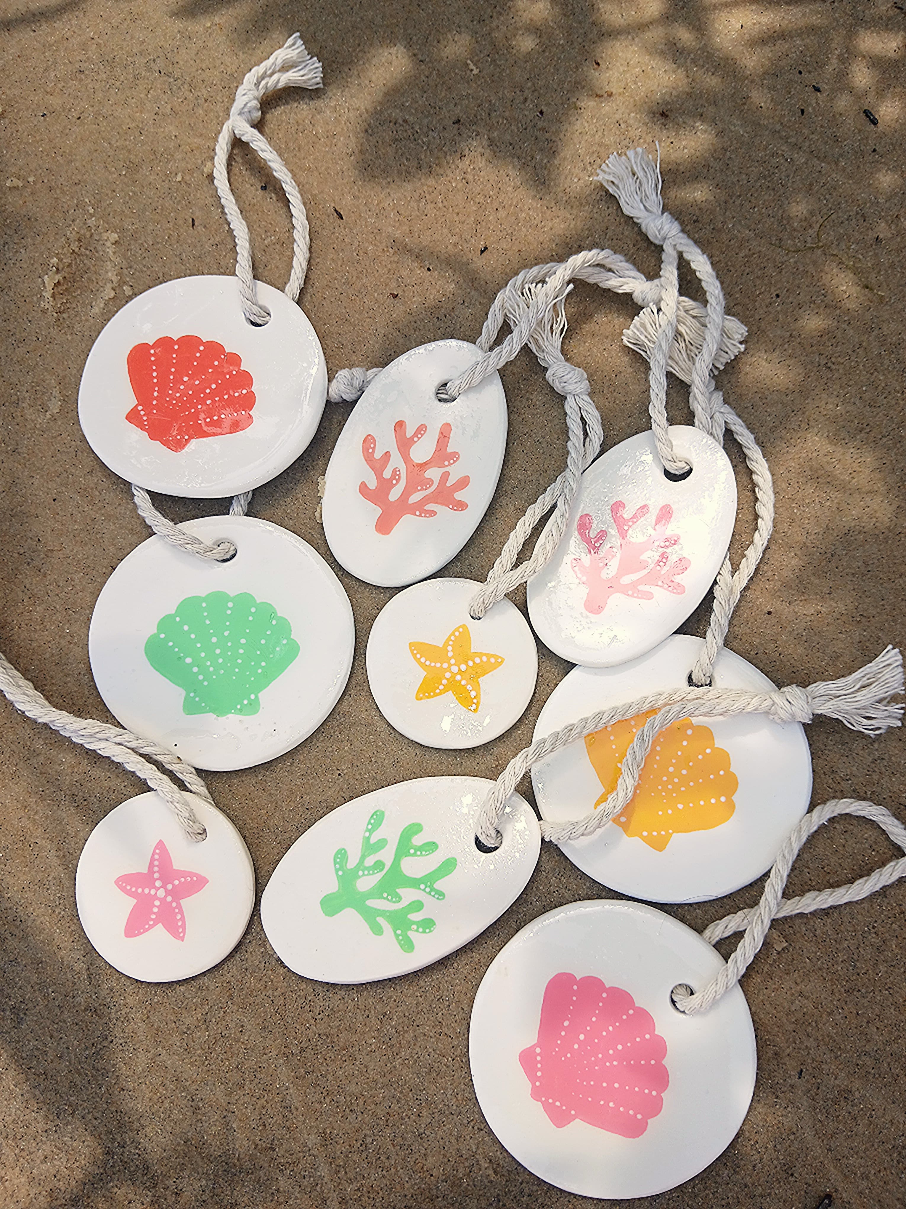 Suspensions corail, étoile de mer et coquillage en rose, vert, jaune et corail, posées sur le sable